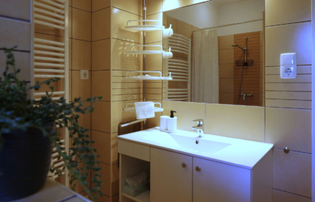 Bathroom with beige tiled walls, white sink, large mirror, and a wall-mounted towel warmer; shower area with curtain visible in the background.